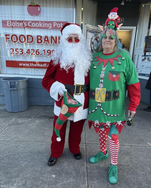 Santa and his elf distributing toys and treats to visitors at Eloise’s Cooking Pot Food Bank during a holiday event.